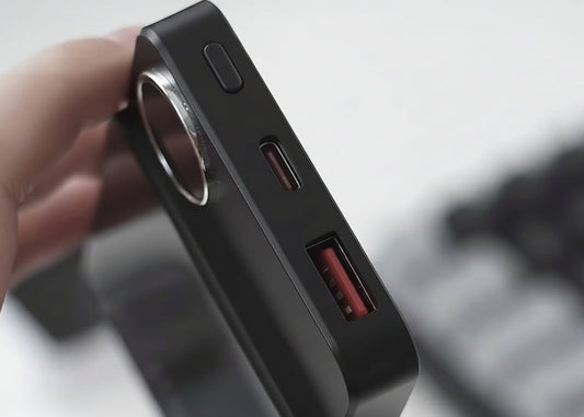 A close-up of a hand holding a black rectangular electronic device, showing its side ports including a USB-C and USB-A port with red accents.