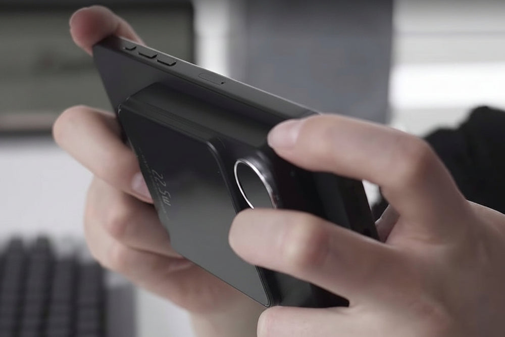 A close-up of a person holding a slim black electronic device, likely a portable media player or gaming console, with their thumbs resting on the front.